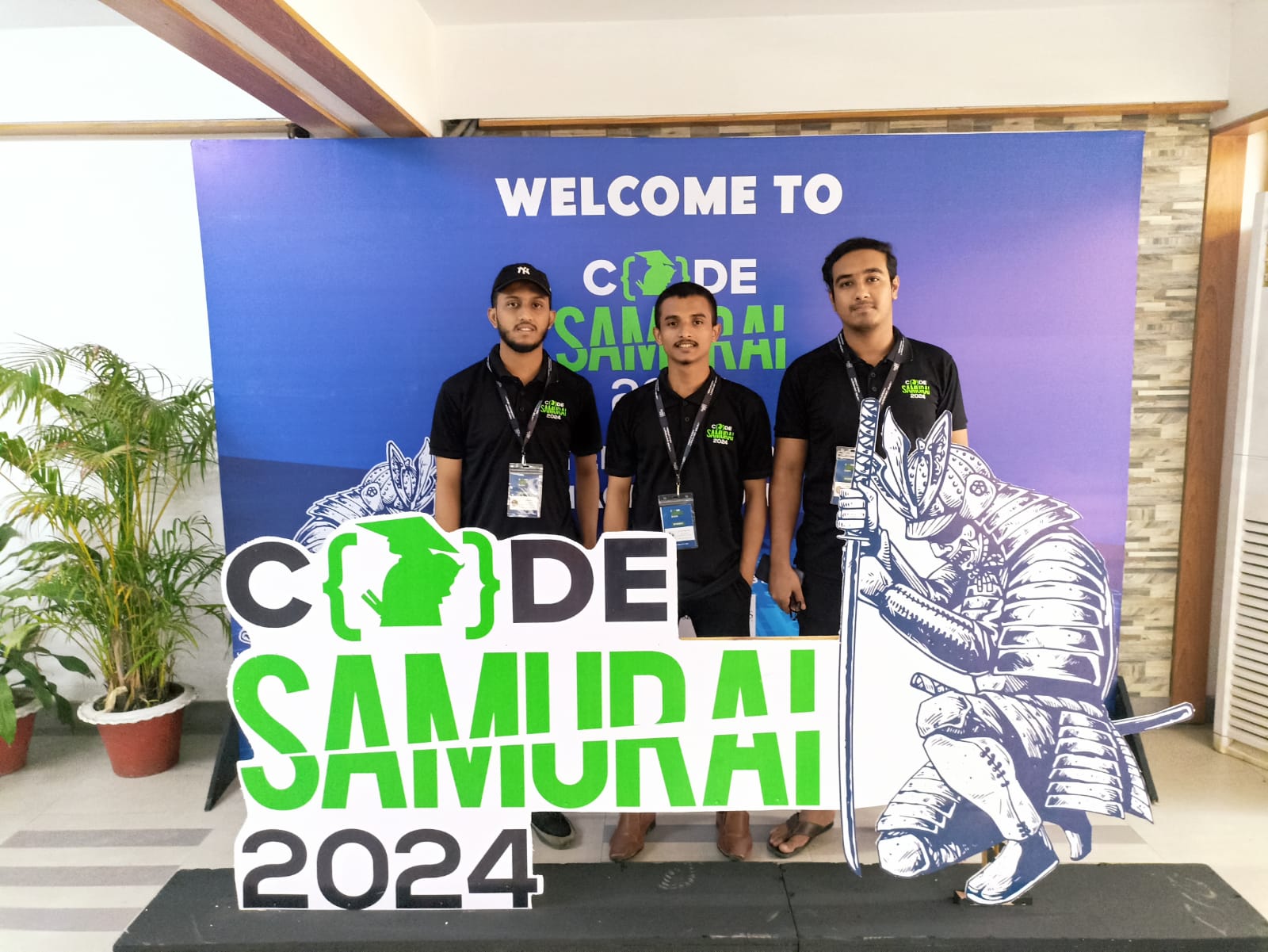 Three team members at the Code Samurai 2024 backdrop at Dhaka University.